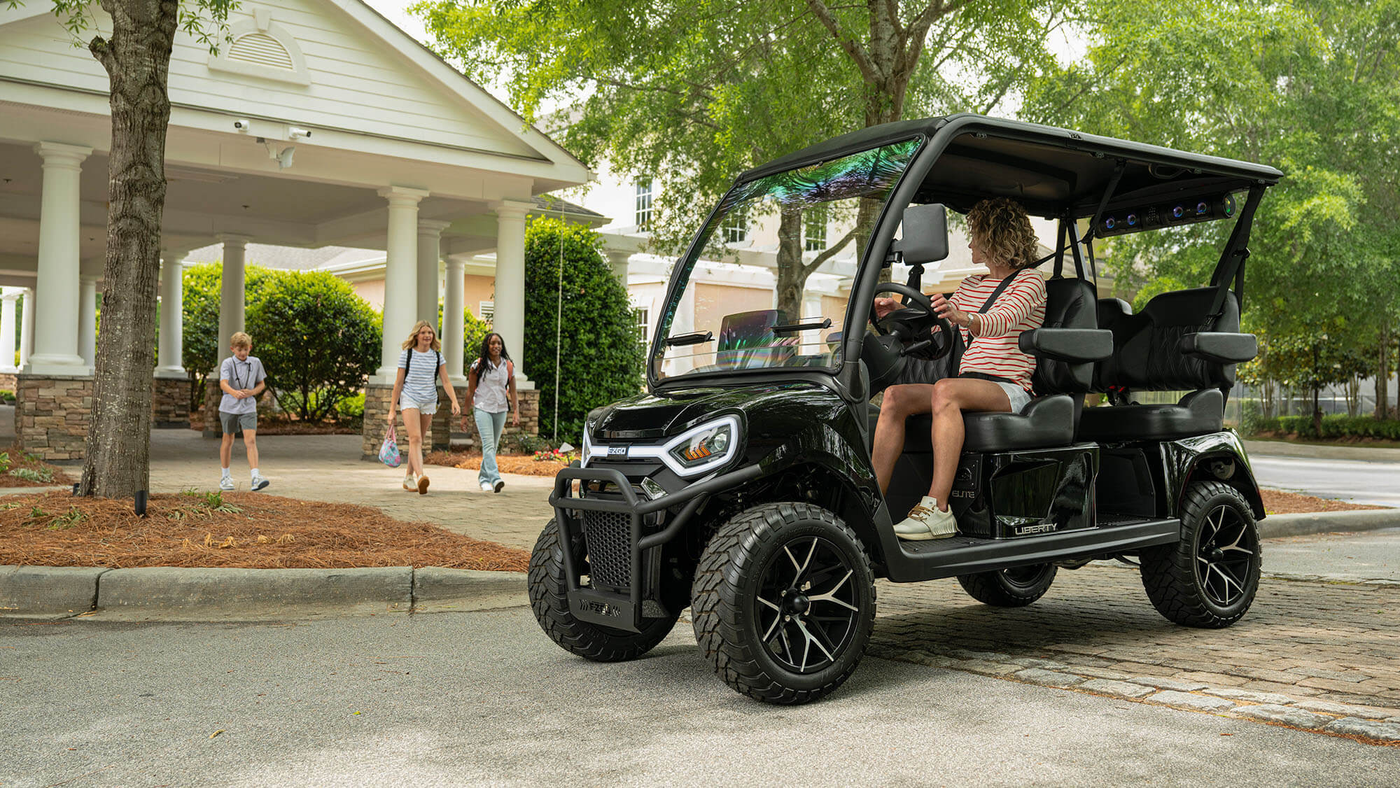 01 Best Golf Carts 2026 EZGO Liberty 4F Black 2027 EZGO Liberty 4F golf cart with four forward facing seats driving through a neighborhood