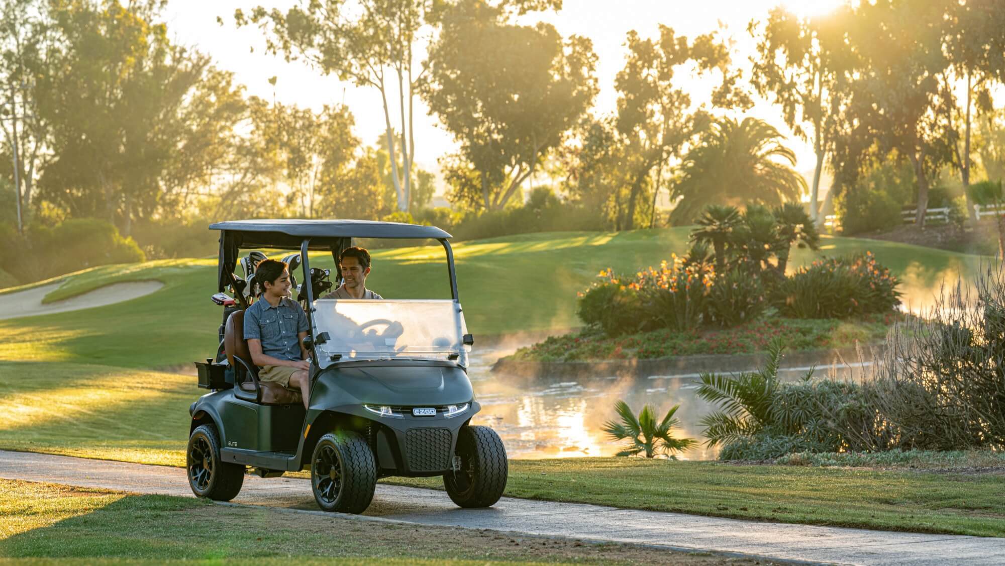 04 Best Golf Carts 2026 EZGO RXV 2 Two golfers driving a 2026 EZGO RXV 2 golf cart on a course path at sunrise