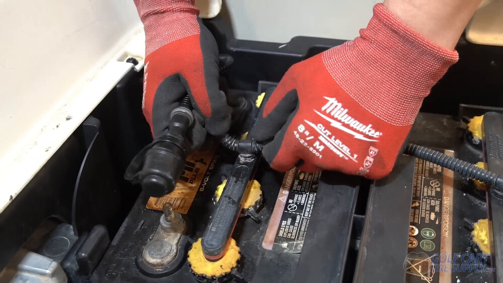 Single point watering system on a Club Car Tempo Gloved hands pulling the single point watering line off the lead-acid batteries in a 2019 Club Car Tempo golf cart