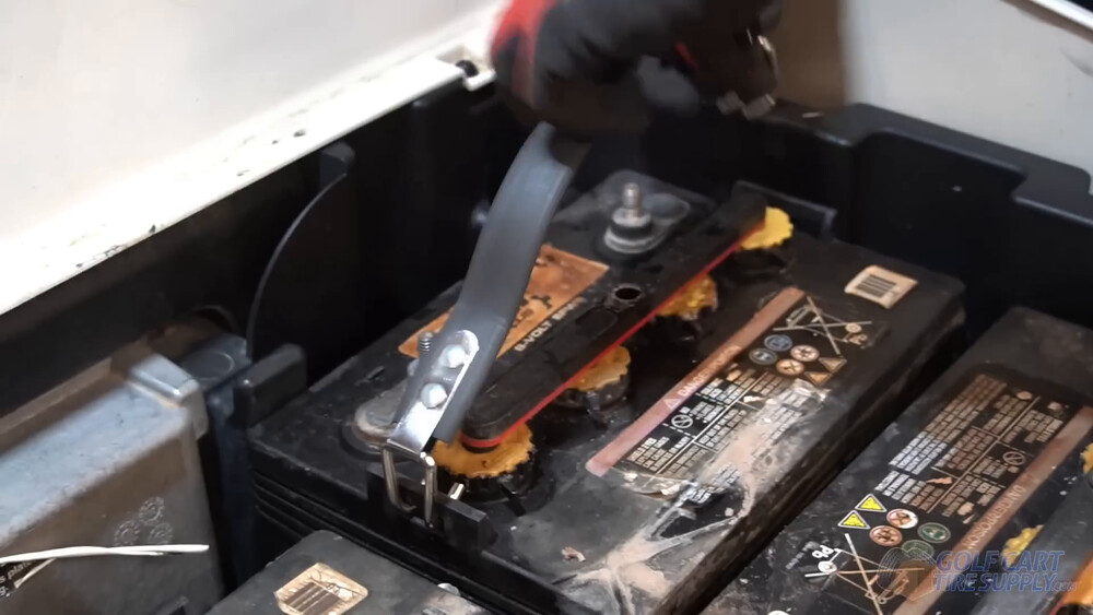 Battery strap on a Club Car Tempo lead-acid battery Battery strap hooked under the end tabs of a lead-acid battery in a 2019 Club Car Tempo golf cart