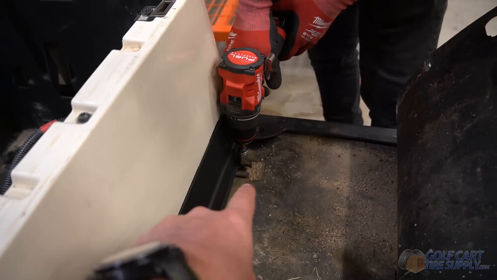 Removing the Club Car Tempo kick panel bolts Cordless driver removing a lower kick panel bolt under the seat of a white 2019 Club Car Tempo golf cart