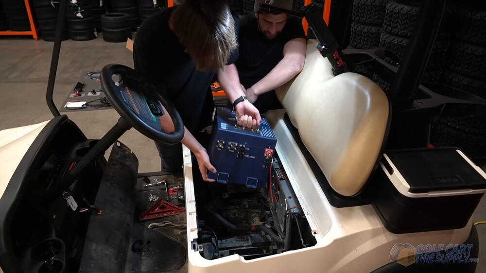 Lowering the lithium battery into a Club Car Tempo Two people lowering the ALLIED 48V lithium battery into the battery bay of a white 2019 Club Car Tempo golf cart