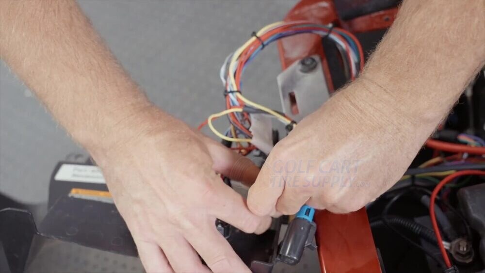 Disconnecting the battery communication plug on an EZGO RXV ELiTE Gen 1 Hands unplugging the blue battery communication plug on a Gen 1 EZGO RXV ELiTE